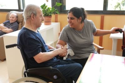 Persona ajudant a una altra persona en cadira de rodes, donant-li suport